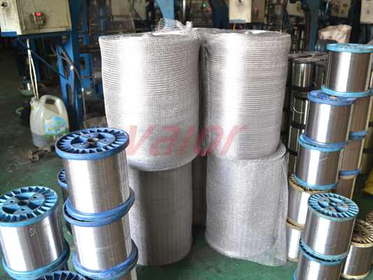 Four rolls of knitted mesh are placed among a pile of stainless steel wire spools.